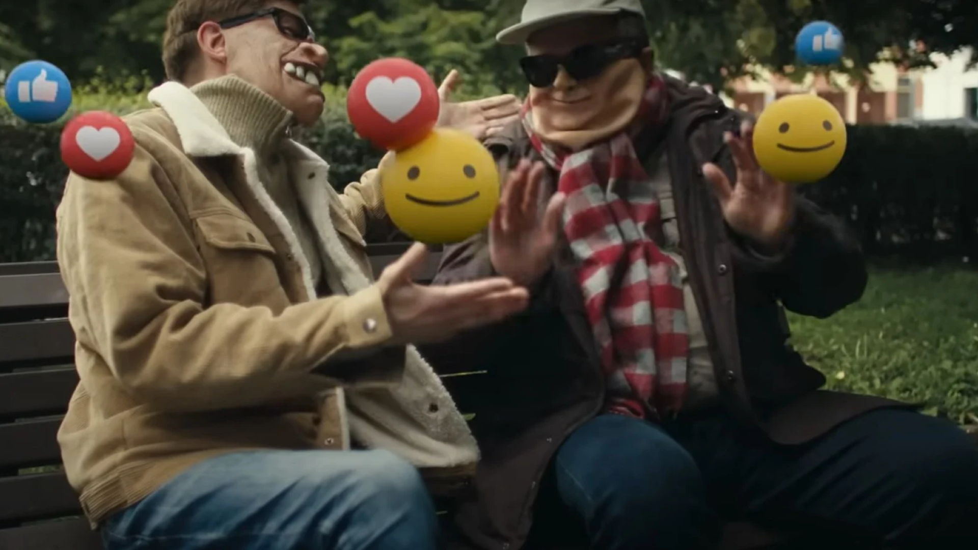 Joyful image showing two elderly men on a park bench, playfully juggling emojis such as a heart, a thumbs up, and a smiling face. They are enjoying a lighthearted moment, surrounded by a serene park setting. This visual metaphor creatively highlights the positive impact of social media interactions among seniors