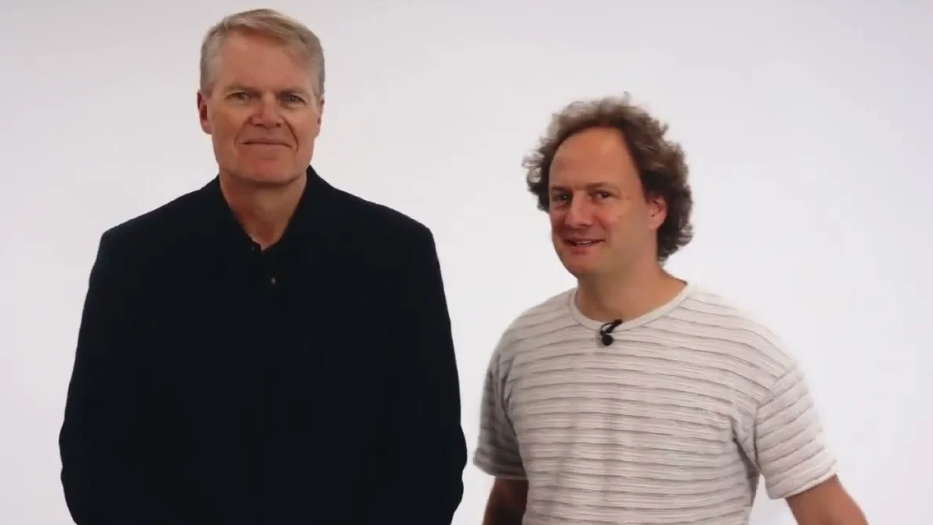 Portrait of two men - Mike Seymour, Digital Humans Researcher and leader of Motus Lab, and Grant Reaber, the Chief Research Officer at Respeecher -  standing side by side against a plain white background. On the left, a man in a dark navy sweater smiles confidently, while on the right, a man in a striped t-shirt gives a friendly, amused expression. This image represents a collaboration or discussion between professionals, likely in a tech or creative industry.