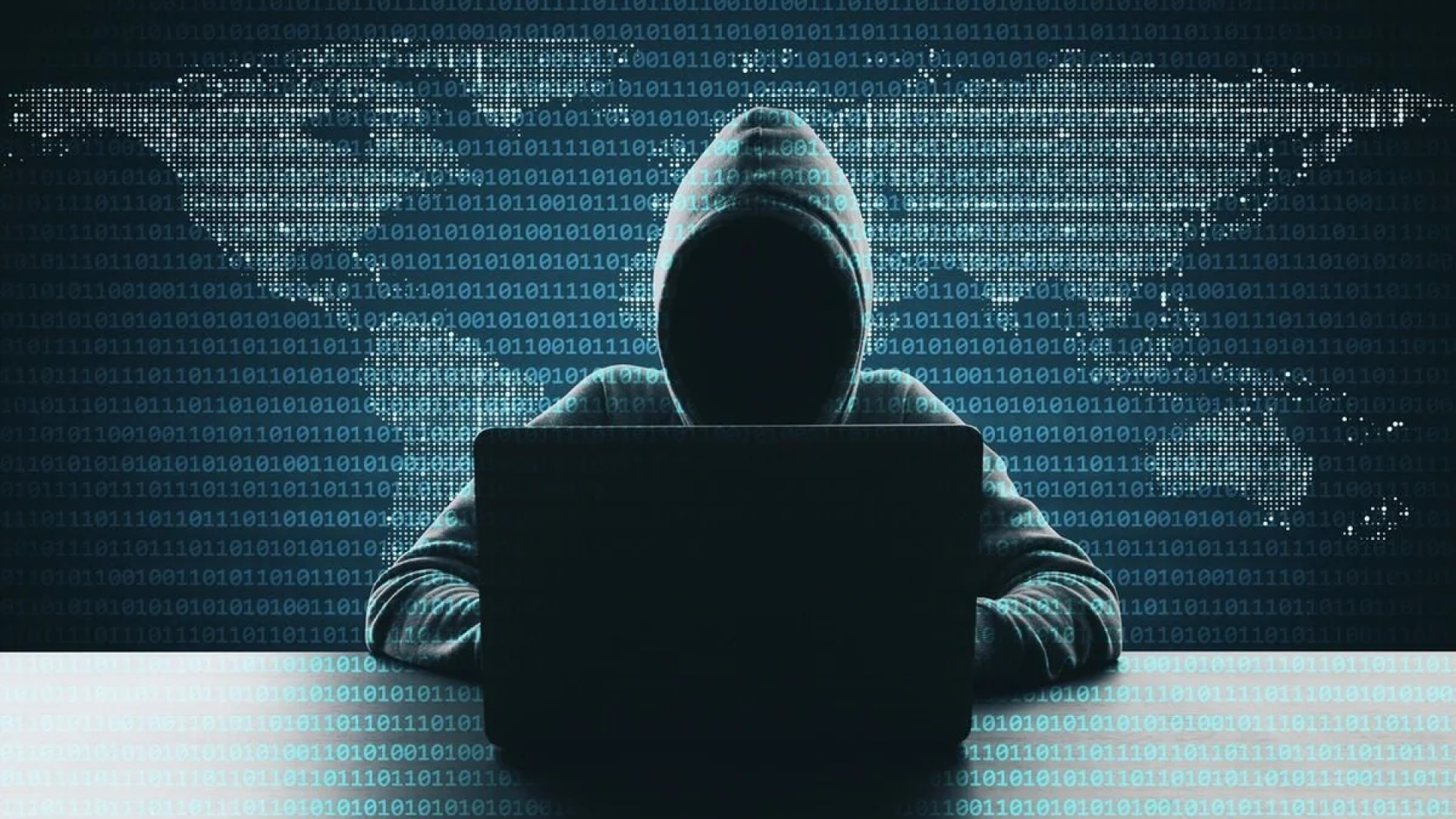 Mysterious figure in a hoodie working on a laptop with a digital map of the world in the background, representing a cybersecurity concept in a dark, data-filled environment